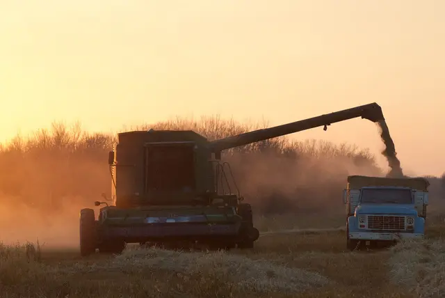 Combine unloading grain into a truck at sunset
